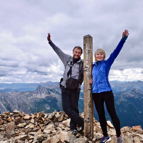 Two people celebrating at the top of a mountain with a scenic view.