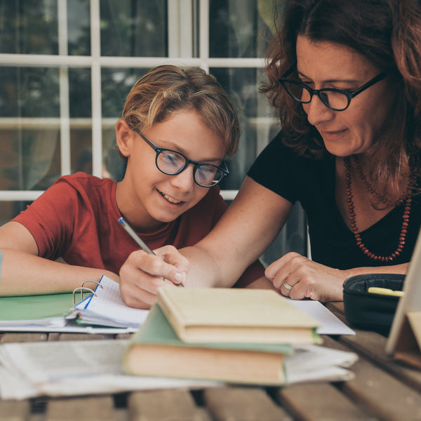 Woman and child sitting at a table with books and a laptop, engaged in an activity.